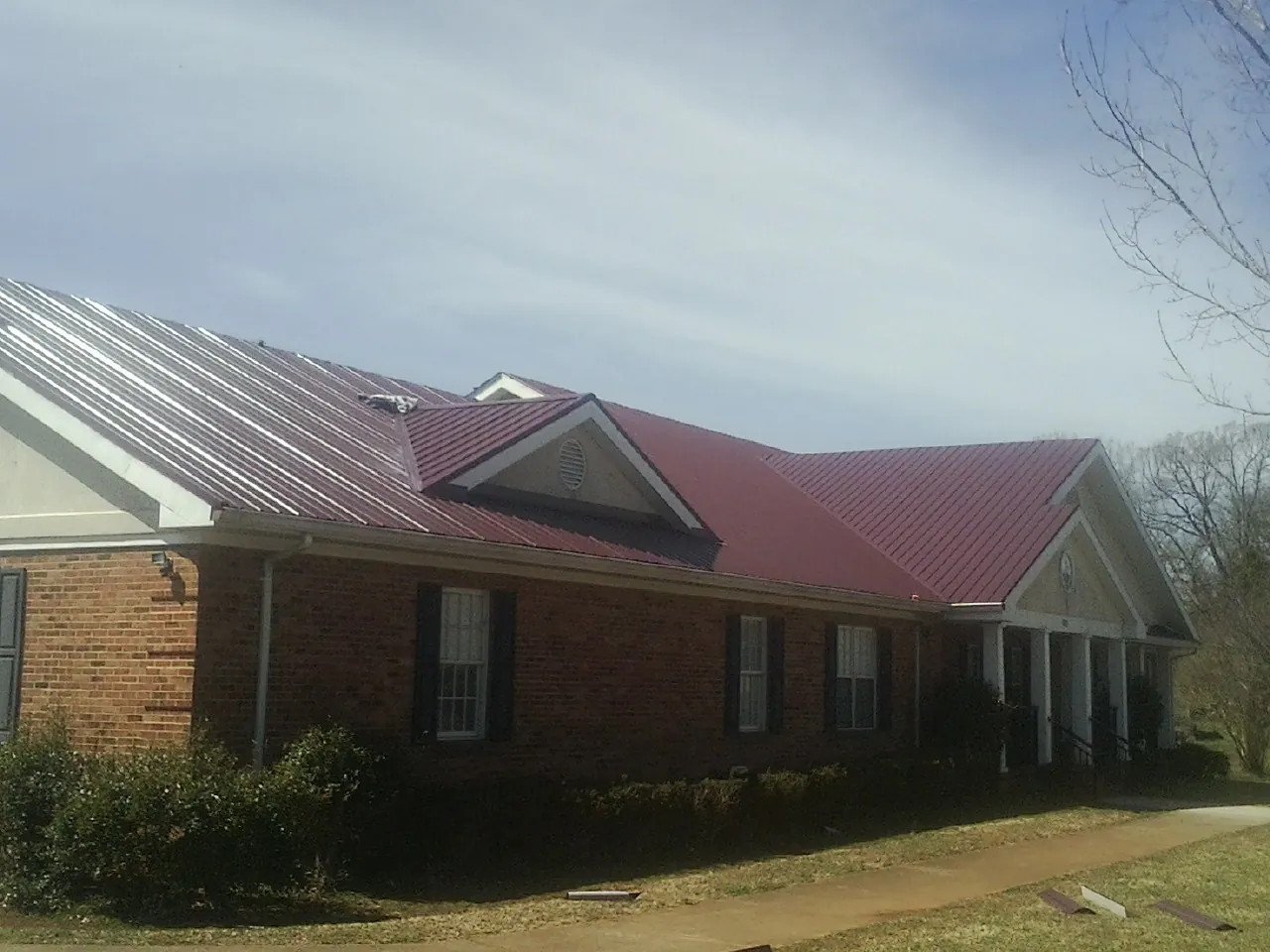 Red metal roof with gabled entries on a long brick building, from a Hail Damage Roof Repair job in Rembert