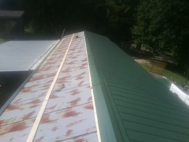 Old rusted panels beside newly installed green metal roofing — Wind Damage Roof Repair by Roofing Brothers in Rembert