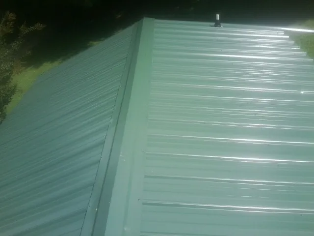 New green metal panels meeting at the ridge of a roof — Flat Roof Repair work by our crew in Rembert