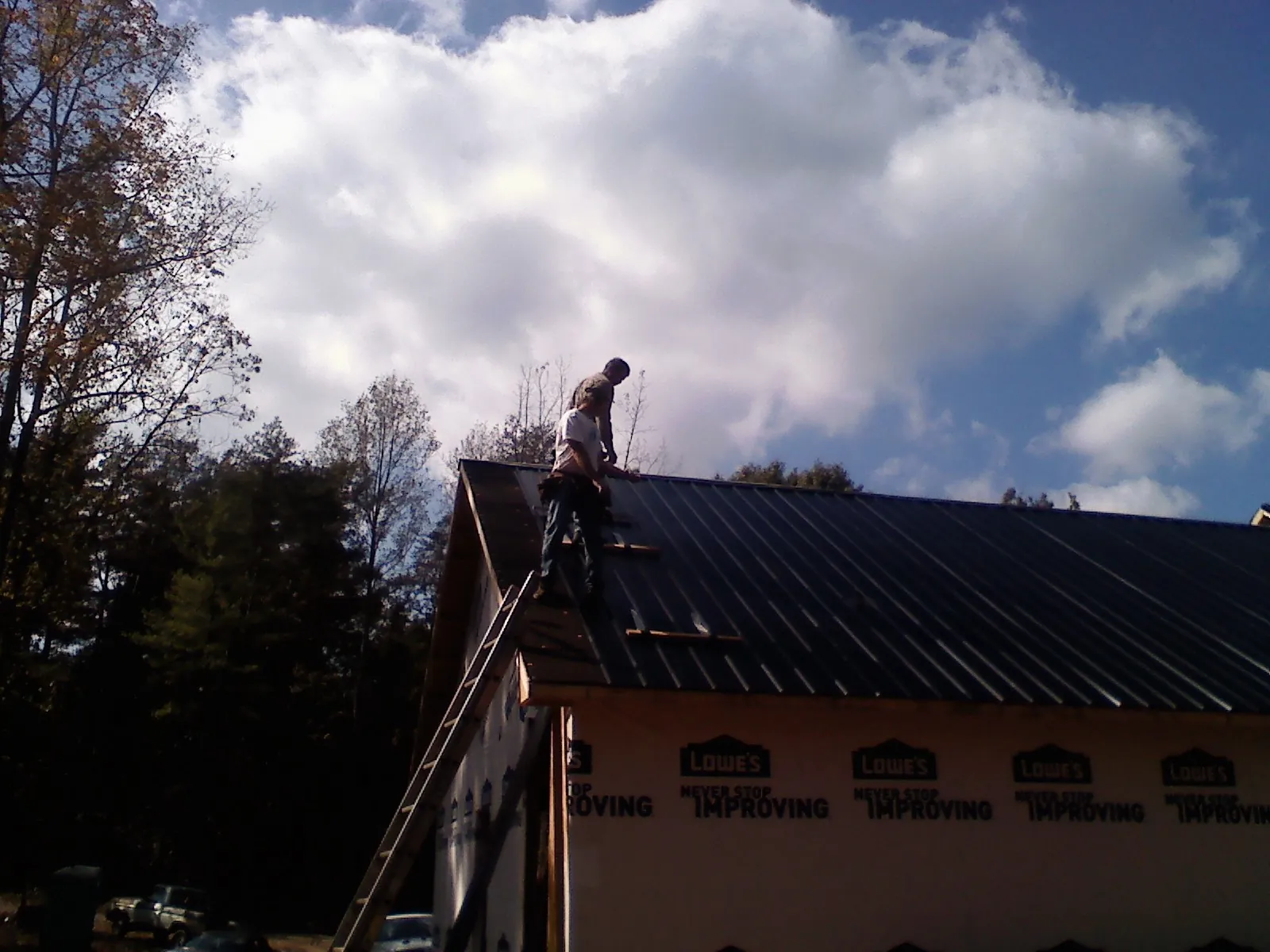 Roofer fastening dark metal panels high against a cloudy sky, from a Roof Inspection job in Rembert