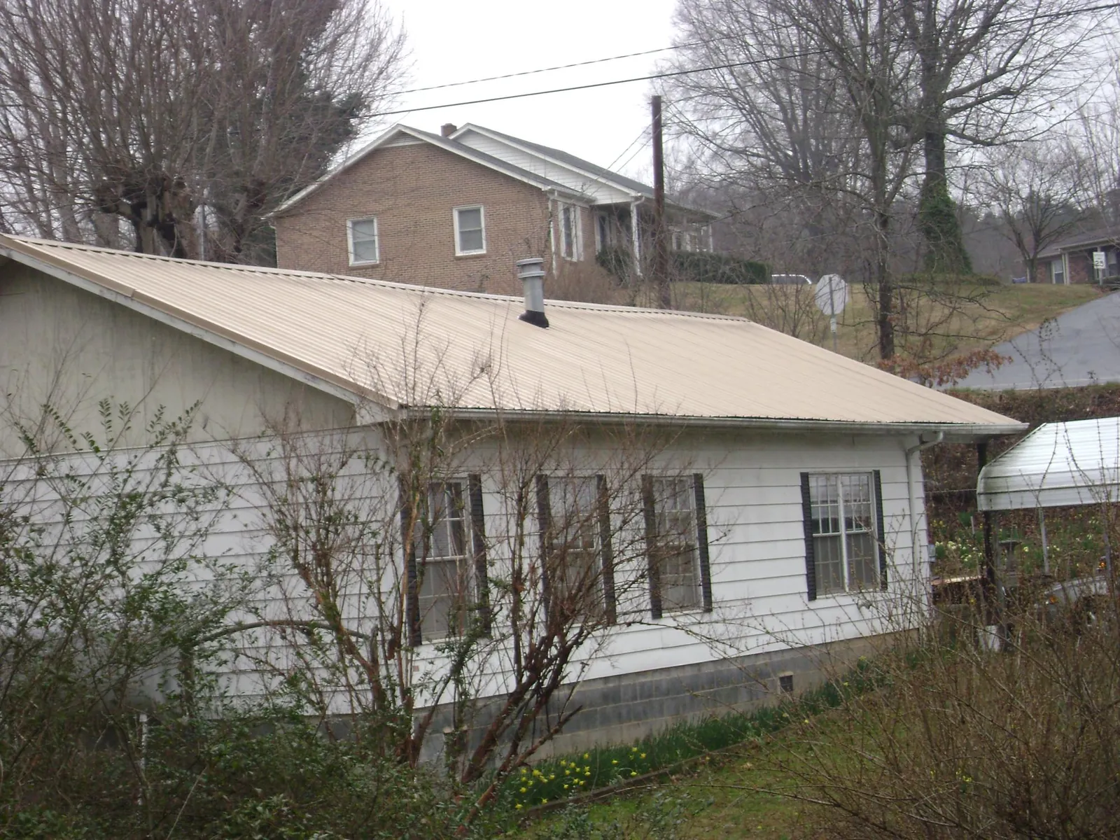 Tan metal roof on a white sided house set into a hillside — Commercial Roofing by Roofing Brothers in Rembert